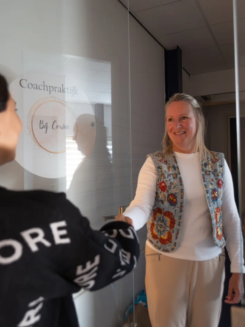 Corine verwelkomt een bezoeker bij de deur van haar coachpraktijk.